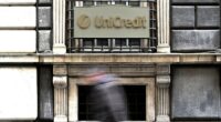 A person walks past a sign with the logo of the Italian bank UniCredit on its bank branch in central Genoa,