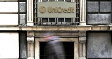 A person walks past a sign with the logo of the Italian bank UniCredit on its bank branch in central Genoa,