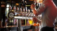Barista in the pub pouring beer drink into glass for the customer.