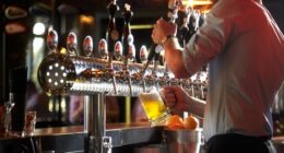 Barista in the pub pouring beer drink into glass for the customer.