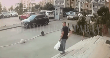 Man carrying a bag walks up steps towards a building with cars parked in the background.