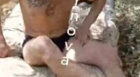 A shirtless soldier sits on a blanket, appearing to be in distress.