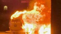 Car engulfed in flames near a building.