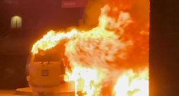 Car engulfed in flames near a building.
