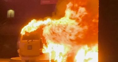 Car engulfed in flames near a building.