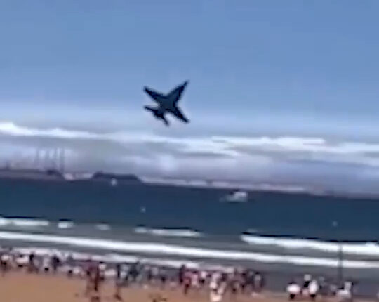 Jet plane flying low over a crowded beach.