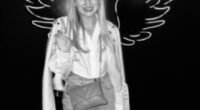 Black and white photo of Georgia Harry posing in front of a neon wing backdrop.