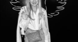 Black and white photo of Georgia Harry posing in front of a neon wing backdrop.