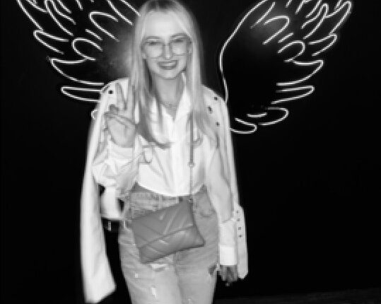 Black and white photo of Georgia Harry posing in front of a neon wing backdrop.