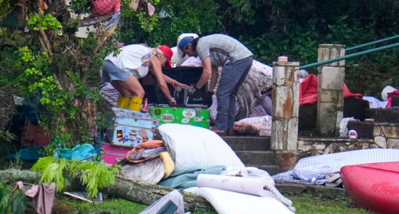 Two adults sweep through the belongings of campers in the aftermath of the flash flood