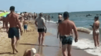 Crowded beach with people walking on the sand and in the water.