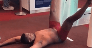 Man in red underwear lying on the floor at an airport gate.