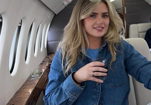 Woman seated in a private jet with two men in the background.