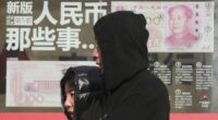 Residents walk past board highlighting the security markers on the latest Yuan note