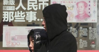 Residents walk past board highlighting the security markers on the latest Yuan note