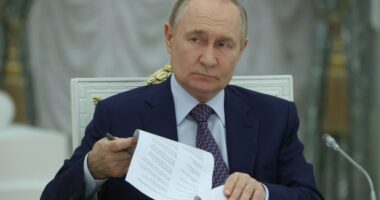 Vladimir Putin reviewing documents at a meeting.