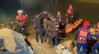 Rescue workers assisting a diver near a body of water.