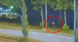 Nighttime security camera footage of a person running along a road.
