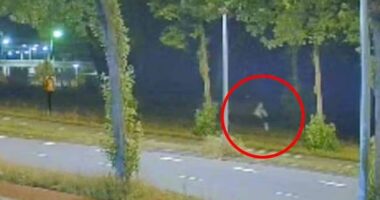 Nighttime security camera footage of a person running along a road.