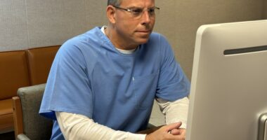 Erik Menendez with gray hear before a computer, wearing prison clothes.