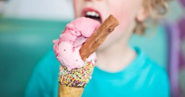 Child eating strawberry ice cream cone with sprinkles and a chocolate bar.