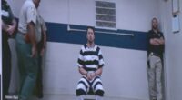 Screenshot of Jaxon Neil in a jail jumpsuit, flanked by officers.