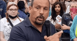 Man speaking into microphone at a protest.