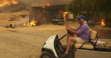 A resident rides a golf cart as he exits his property while the Canyon Fire burns in Hasley Canyon, California.