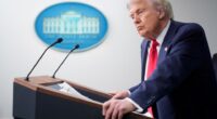 President Donald Trump at a podium listening to a reporter's question.