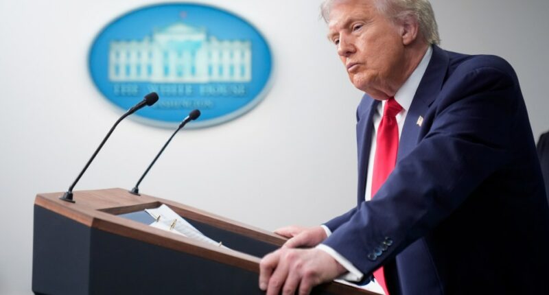 President Donald Trump at a podium listening to a reporter's question.