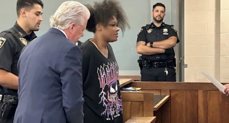 A woman in court, flanked by police officers and a man in a suit.