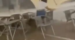 A waitress struggles to hold onto a patio umbrella during a strong windstorm.