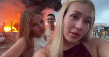 Two young women filming themselves in front of a burning oil depot.