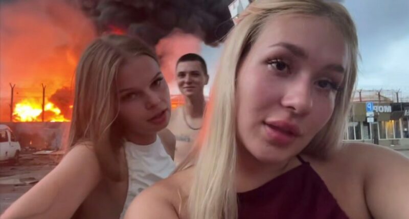 Two young women filming themselves in front of a burning oil depot.
