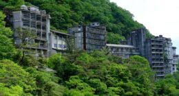 Overgrown abandoned hotel buildings on a hillside.