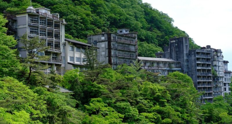 Overgrown abandoned hotel buildings on a hillside.