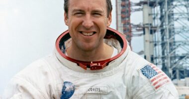Portrait of Jim Lovell, Apollo 13 commander, in a spacesuit holding a moon globe.