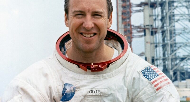 Portrait of Jim Lovell, Apollo 13 commander, in a spacesuit holding a moon globe.