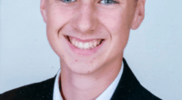 Photo of a smiling boy in a suit and red tie.