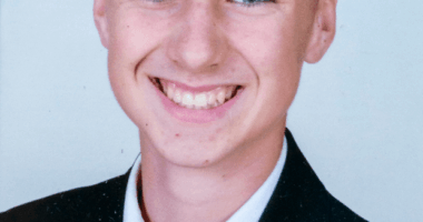 Photo of a smiling boy in a suit and red tie.