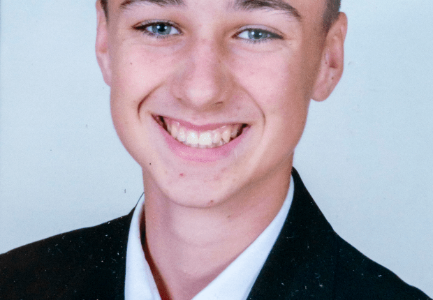 Photo of a smiling boy in a suit and red tie.
