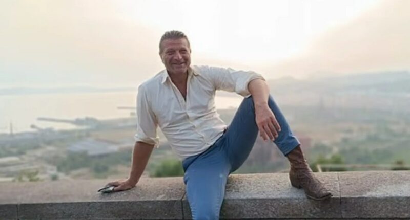 Luigi Di Sarno, 52, sitting on a wall overlooking a city.
