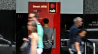 A man uses an NAB ATM as pedestrians walk past.