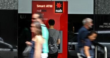 A man uses an NAB ATM as pedestrians walk past.