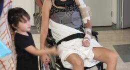 Woman in wheelchair with neck brace and arm sling, surrounded by family.
