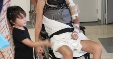 Woman in wheelchair with neck brace and arm sling, surrounded by family.