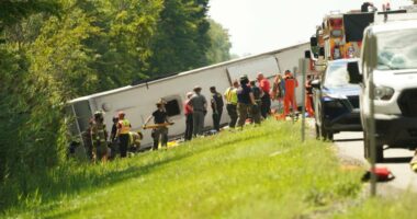 First responders assisting victims at the scene of a rolled-over tour bus.