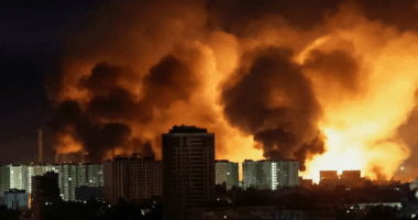 Large fire behind city buildings at night.