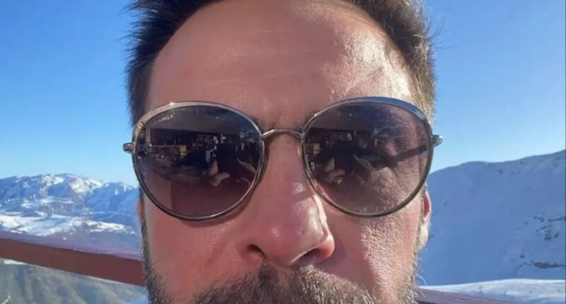 Selfie of a man wearing sunglasses, with snowy mountains in the background.