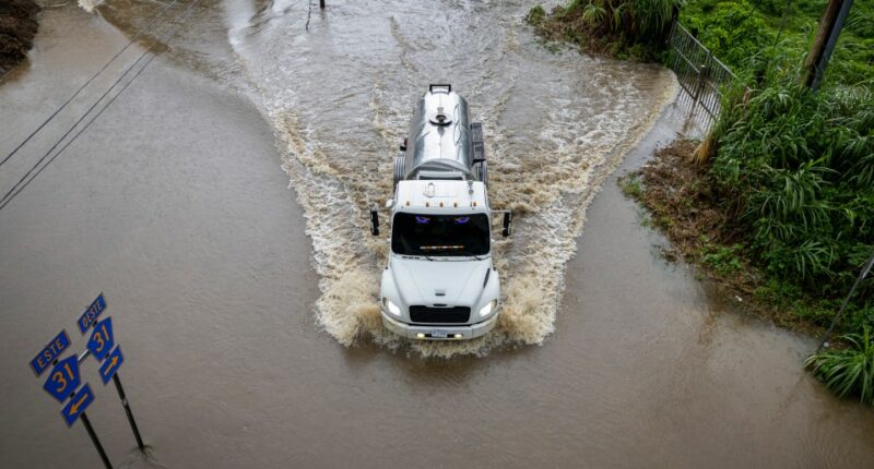 Truck driving through floodwaters on a road.